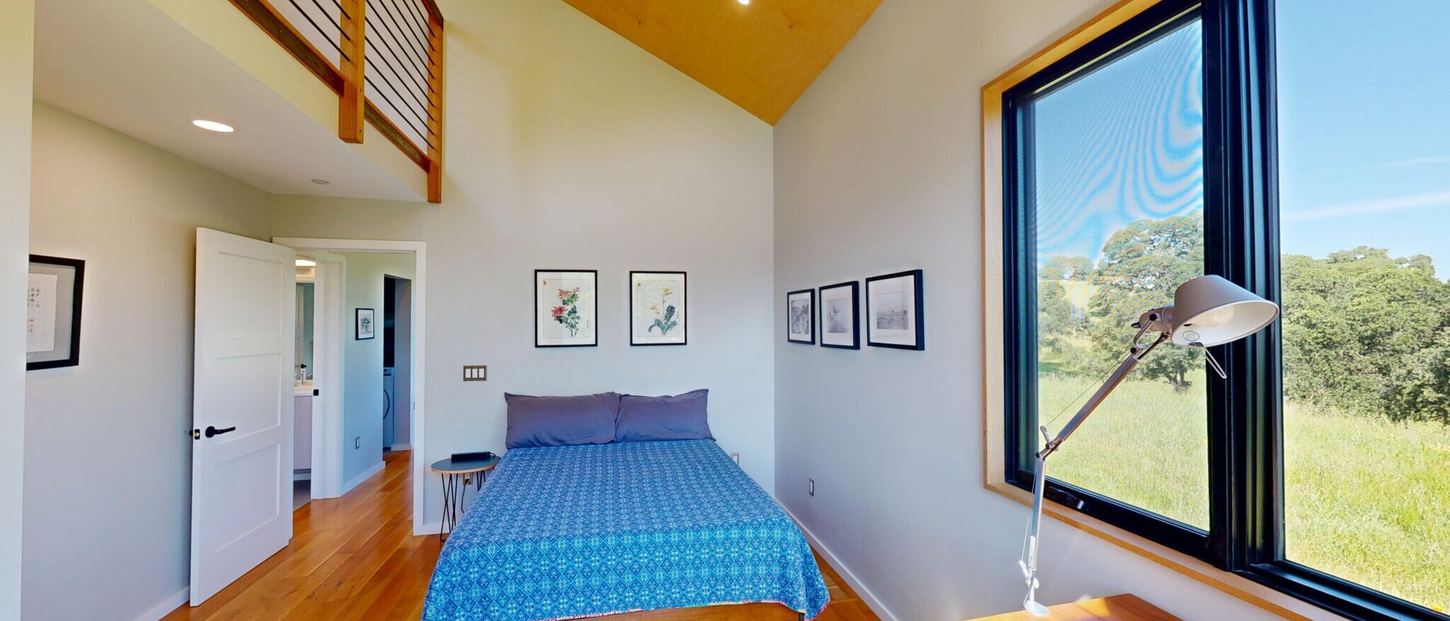 Modern bedroom with open loft and scenic views in a custom Napa home, built by Black Creek Builders, featuring wood floors and high ceilings.