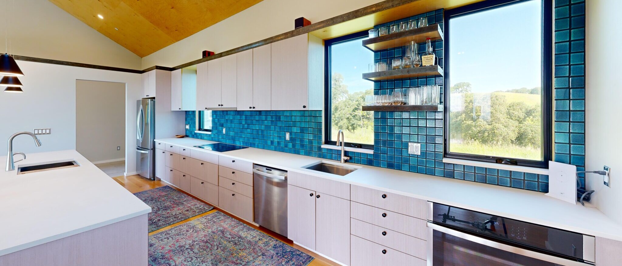 Modern custom kitchen with blue tile backsplash, white countertops, and large windows overlooking Napa landscape, built by Black Creek Builders.