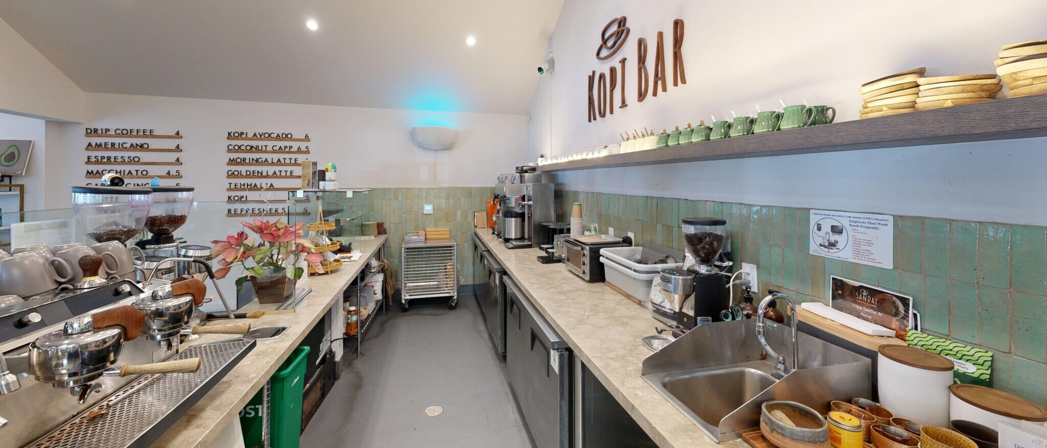 A vibrant and well-equipped coffee bar or cafe by Black Creek Builders, featuring a long counter with multiple coffee machines, blenders, and other preparation equipment. The wall behind the counter has a unique green tiled wainscoting and a menu board displaying drink options like 