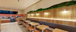 Modern restaurant interior with wood paneling, long banquette seating, and unique lighting and green wall decor, constructed by Black Creek Builders.