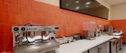 Commercial coffee and beverage station with espresso machine and orange tiled backsplash, part of a restaurant build by Black Creek Builders.